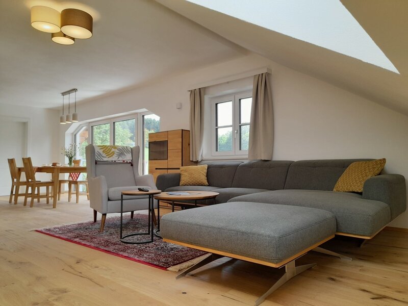 The combined living and dining area of the farmhouse features a large sectional sofa, an armchair, and a wooden dining table.