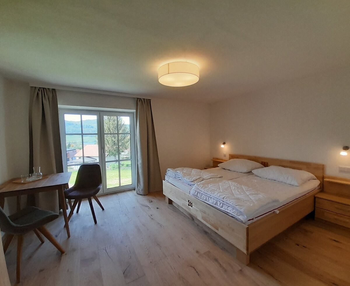 Double bedroom in the farmhouse with a wooden double bed, two bedside tables, a small table with chairs, and a window offering green landscape views.