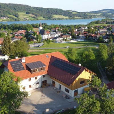 The Farm House, featuring solar panels on its roof, is located in a village setting with a church, overlooking a lake and surrounding green hills.