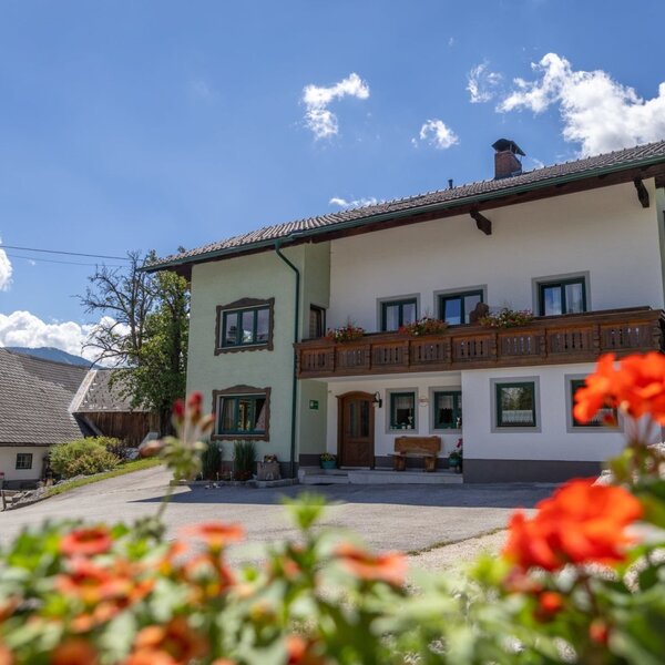 An inviting farmhouse with a traditional wooden balcony and vibrant flowers under a bright blue sky.