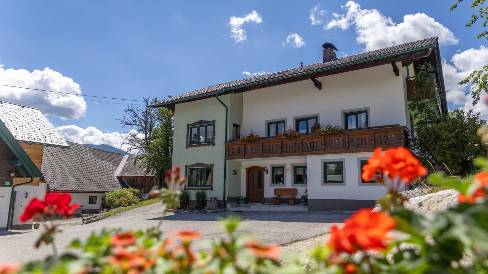 An inviting farmhouse with a traditional wooden balcony and vibrant flowers under a bright blue sky.