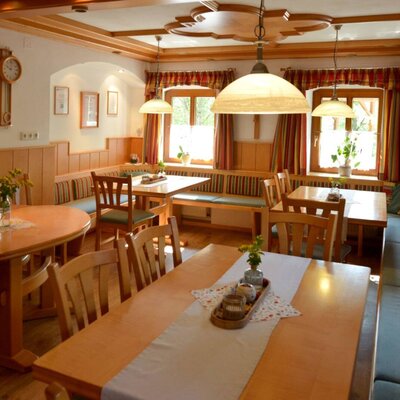 The dining area in the farmhouse with wooden tables, benches, chairs, and a traditional tiled stove.