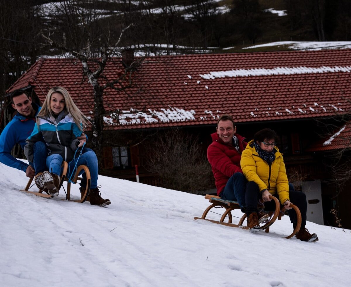 Four people sledding down a snowy slope at the Bauernhof.