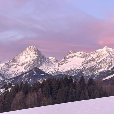 View of snow-covered mountains and forests at sunset from the farmhouse.