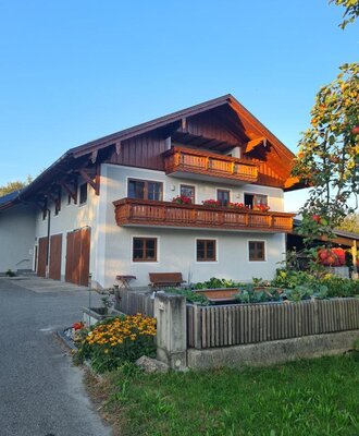 The exterior of the Farm House, featuring a white facade, wooden balconies, and a garden with flowers and raised vegetable beds.