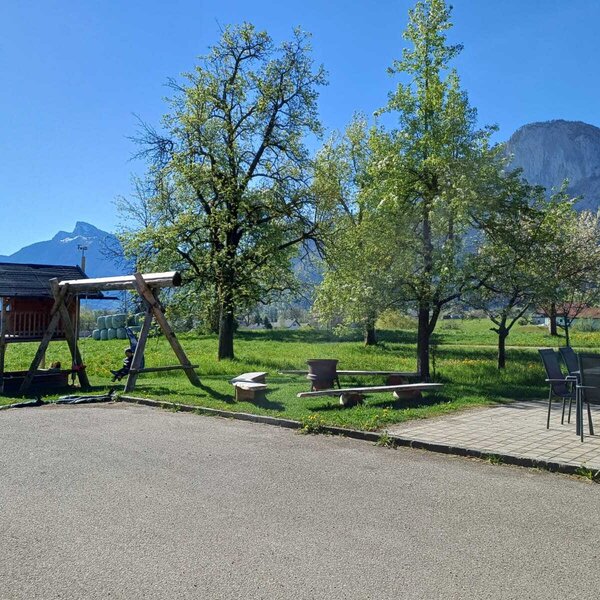 The children's playground with a playhouse and swing, and outdoor seating at the farmhouse, overlooking the surrounding meadows and mountains.