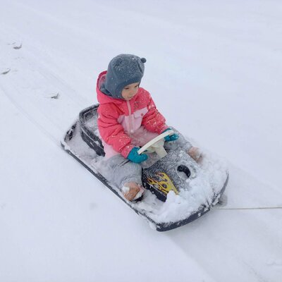 A child on a sled in the snow, illustrating winter activities available at the farmhouse.