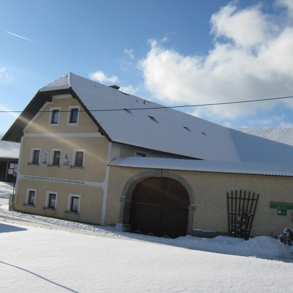The farmhouse exterior covered in snow, featuring a traditional design with a large arched wooden entrance.
