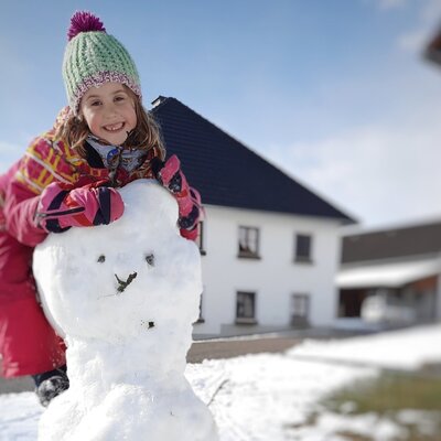 A child building a snowman in the snow at the farm house.