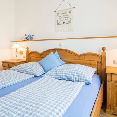 Double bedroom in the Farm House, featuring a wooden bed frame, two bedside tables with wall-mounted lamps, and blue and white checkered bedding.