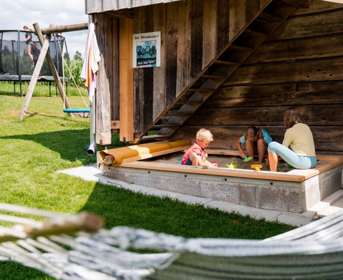 The farmhouse features an outdoor play area with a sandbox, trampoline, and swing set, alongside a hammock for relaxation.