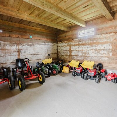 A selection of children's ride-on toys, including pedal go-karts and toy tractors, in the wooden shed of the farmhouse. ©TVB Mühlviertel Berlinger Justin
