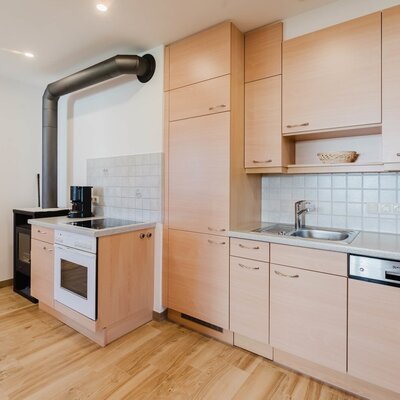 The bright, fully equipped kitchen of the farmhouse apartment, featuring light wood cabinetry and a cozy stove.