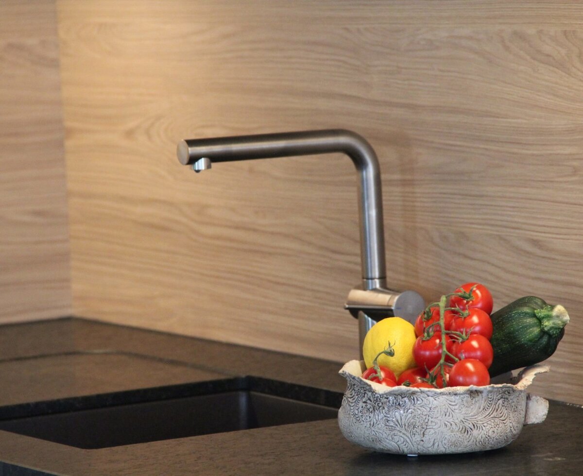 The fully equipped kitchen in the Farm House features a modern sink with a dark countertop, wood-grain backsplash, and a bowl of fresh produce.