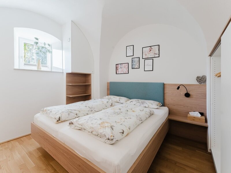 Bedroom of the apartment with a double bed, wooden furniture, built-in shelves, and a wardrobe.