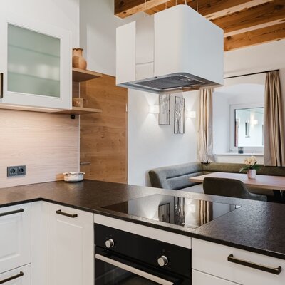 The fully equipped kitchen of the apartment in the farmhouse, featuring an induction hob, oven, a dining area with a corner bench, and wooden ceiling beams.