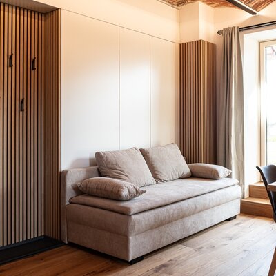 The Farm House features a sofa bed, integrated storage and coat rack with wooden paneling, and a dining area beside a large window.