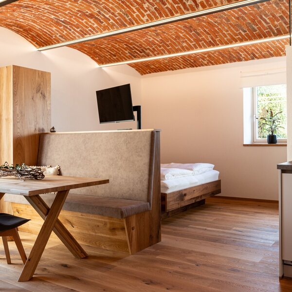 Farm House room featuring a wooden dining table with a bench, a bed, a wall-mounted TV, a kitchenette, and an arched brick ceiling.