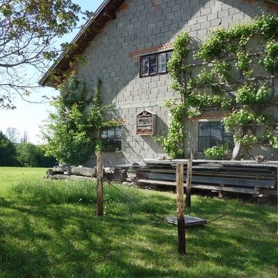 The exterior of the Farm House, featuring a stone block wall with trained climbing plants and an insect hotel, overlooking a large green field and distant trees.