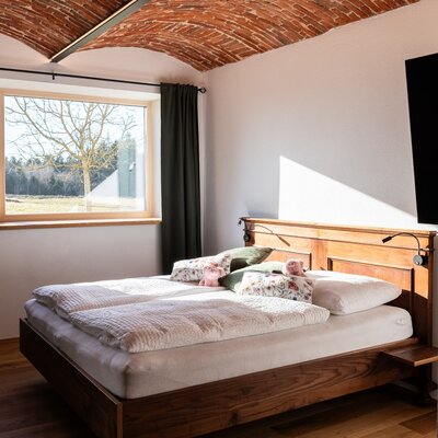 Double bedroom in the Farm House with a wooden bed, a brick vaulted ceiling, a wall-mounted TV, and a window offering field views.
