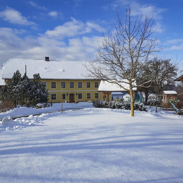 The yellow Farm House exterior and snow-covered grounds, featuring a children's playground.