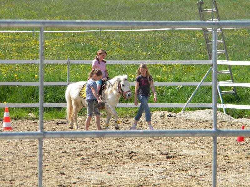 Children learning to ride and lead a pony in the farm house's riding arena.