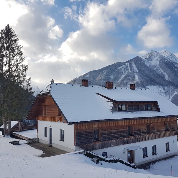 The farm house with its white and wood exterior and snow-covered roof, surrounded by a snowy landscape and mountains.