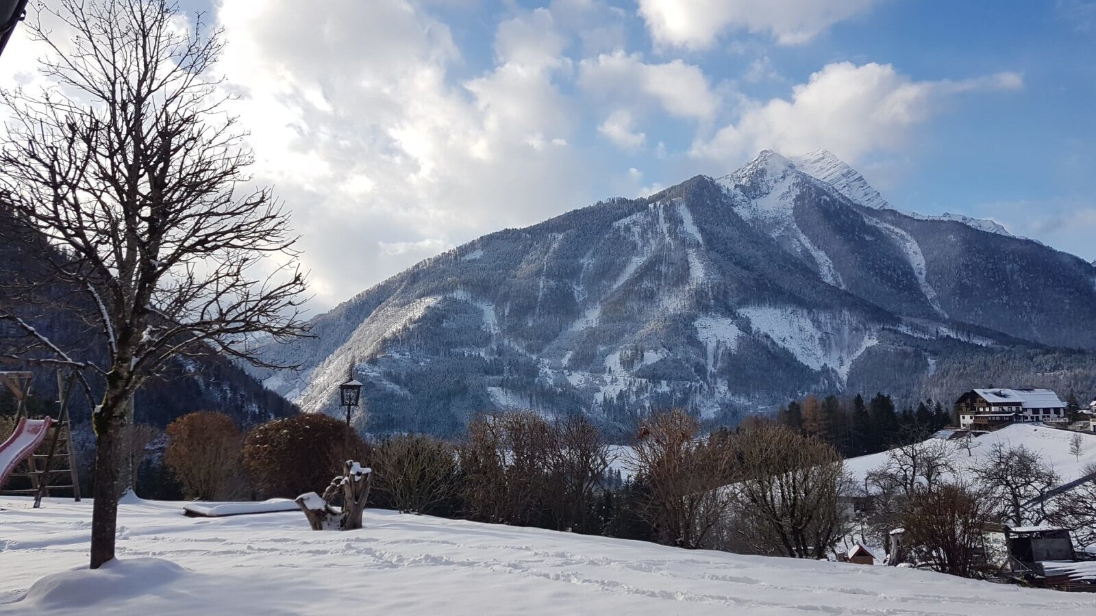 The Farm House's snow-covered outdoor play-area, featuring a slide, is set against a backdrop of snow-capped mountains.