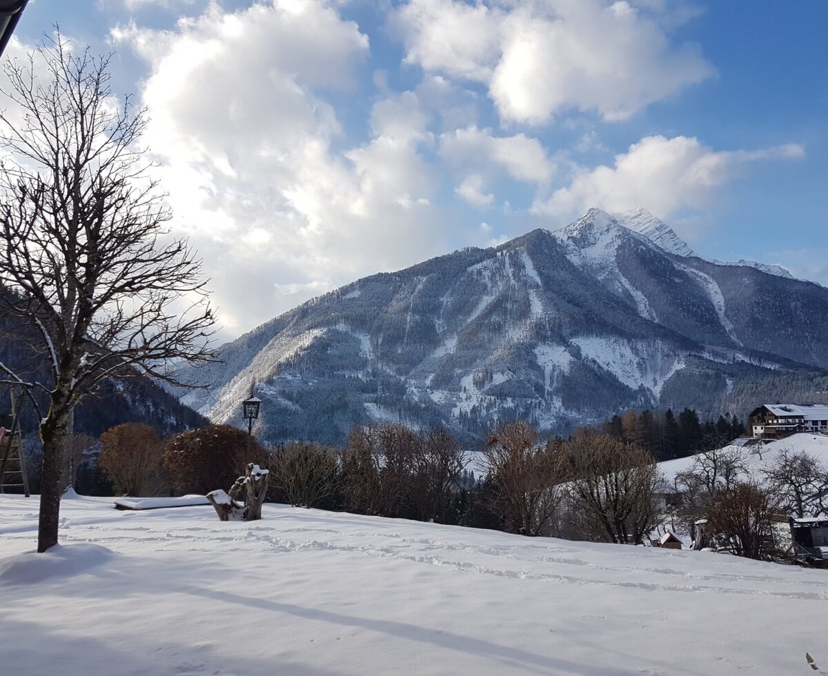 The Farm House's snow-covered outdoor play-area, featuring a slide, is set against a backdrop of snow-capped mountains.