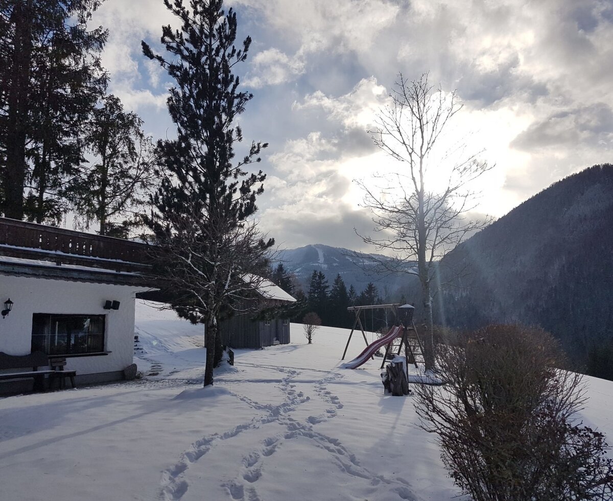 The Farm House exterior in winter, featuring the outdoor play area with a swing set and slide, and mountain views.