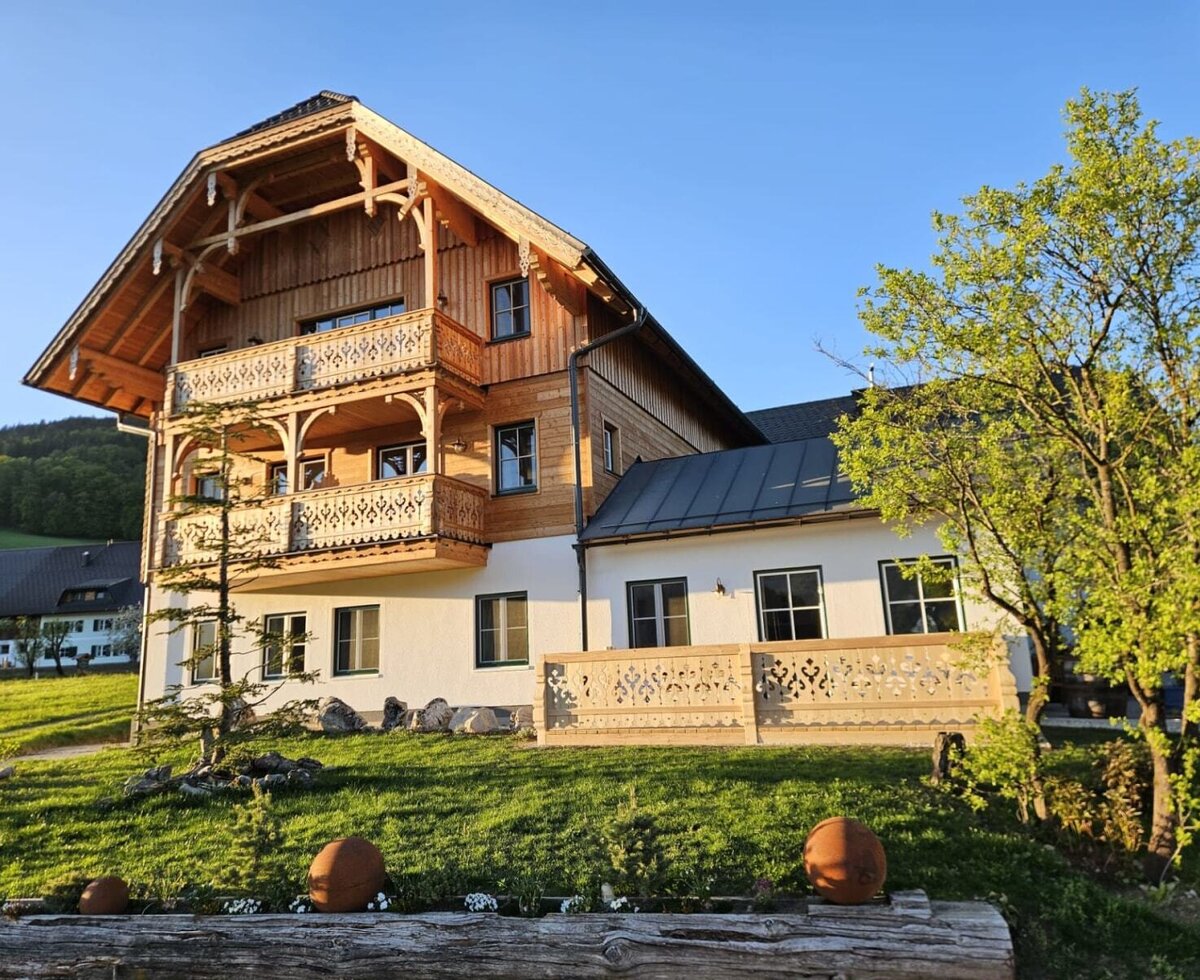 Exterior view of the apartment building featuring a traditional wooden facade, balconies, and a terrace with carved railings.