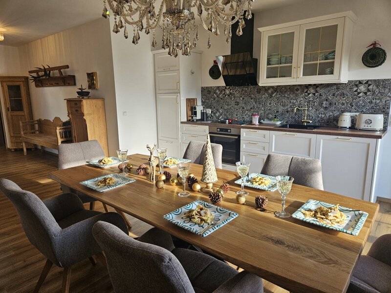 Dining area with a large wooden table and chairs, combined with a modern, fully equipped kitchen in an apartment.