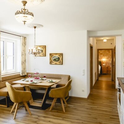 The dining area in the apartment, featuring a corner bench, a set table, and access to the bedroom.
