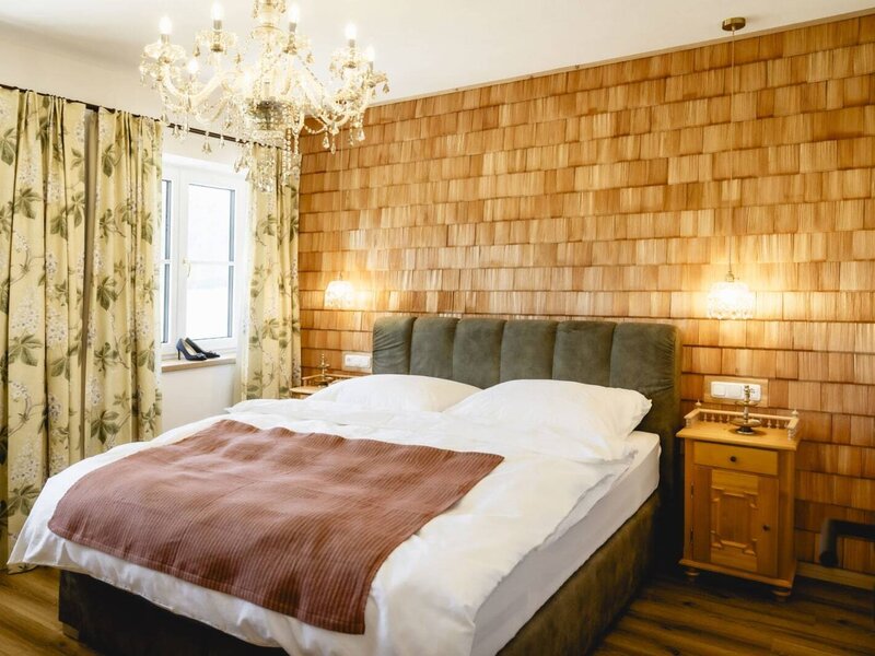 Bedroom in the apartment featuring a double bed, wooden shingle wall, windows with floral curtains, and a chandelier.