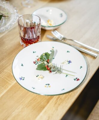 Set table in the Appartements with a plate, cutlery, a glass, and a decoration of wild strawberries and herbs.