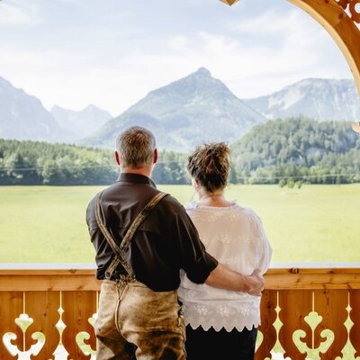 Balcony of an Appartement with traditional wooden railings and a wide view of the mountain panorama and green fields.