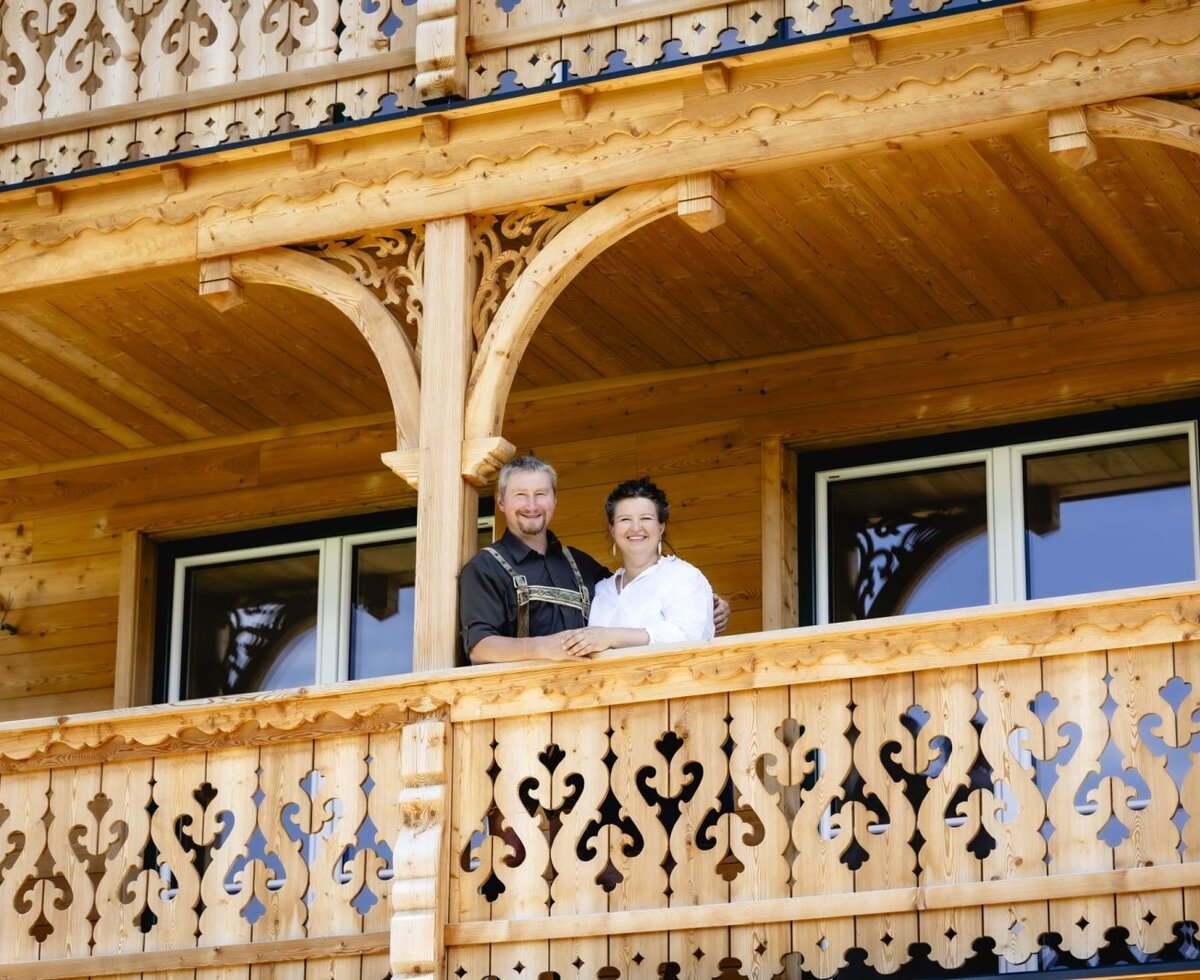 The hosts of the Appartements stand on the balcony with carved wooden railings.