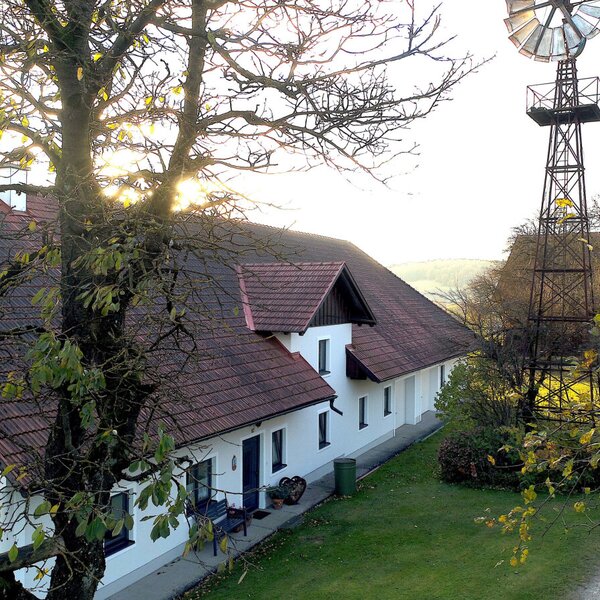 The exterior of the Farm House, featuring its white facade, red tiled roof, and a nearby windmill.