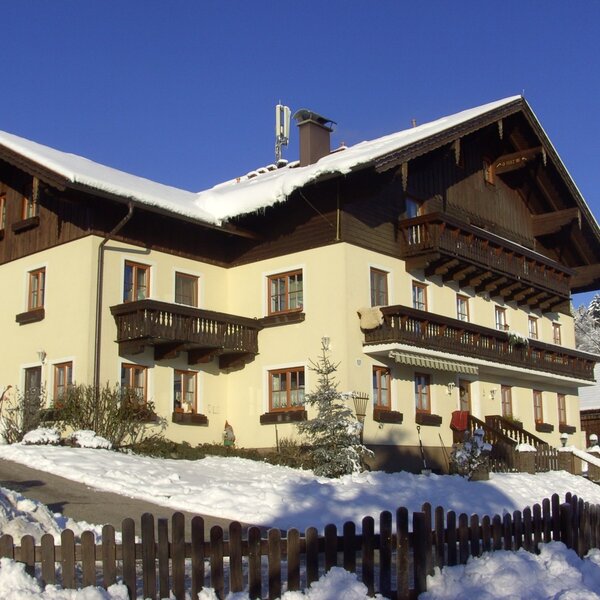 The multi-story farmhouse exterior featuring wooden balconies and a snow-covered roof and grounds.
