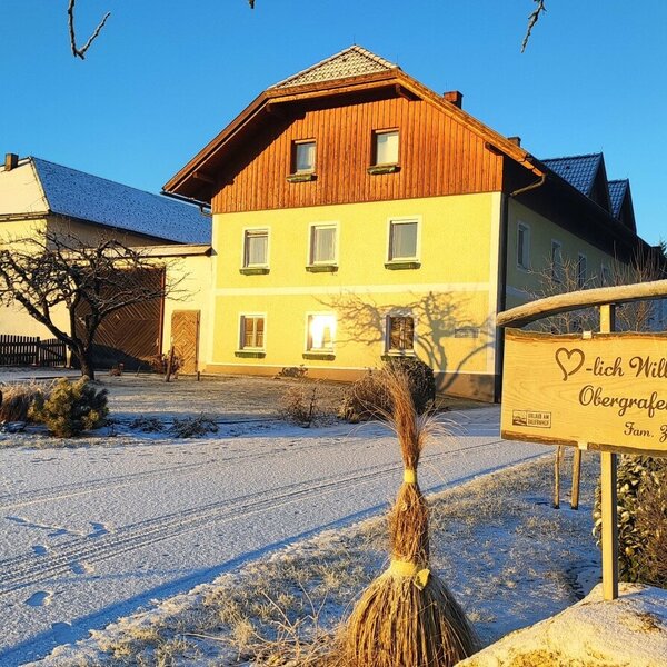 The exterior of the Farm House in a winter setting, featuring a wooden welcome sign and snow-covered grounds.