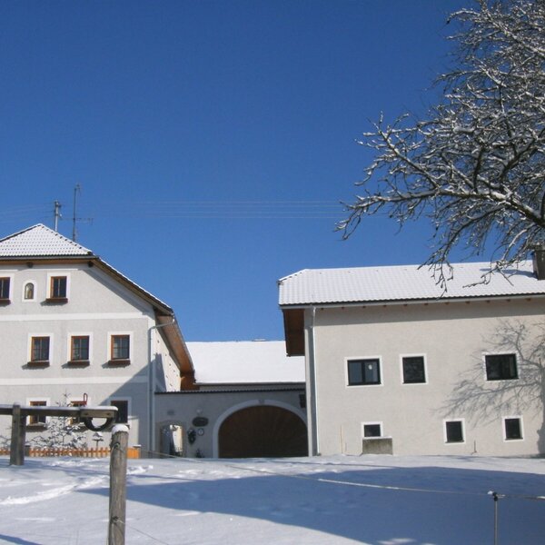 The farm house exterior with snow-covered roofs and grounds under a clear blue sky.