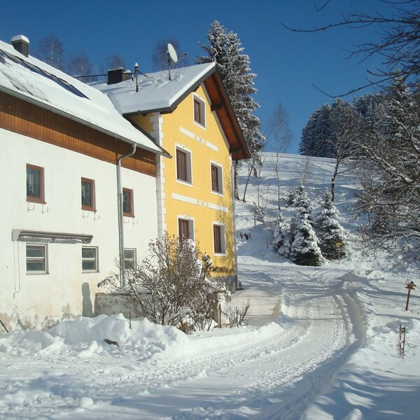 The Farm House exterior in winter, featuring snow-covered buildings and a path leading through the snowy landscape.