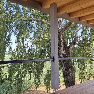 Balcony of the holiday home with a wooden floor and a view of a birch tree and fields.