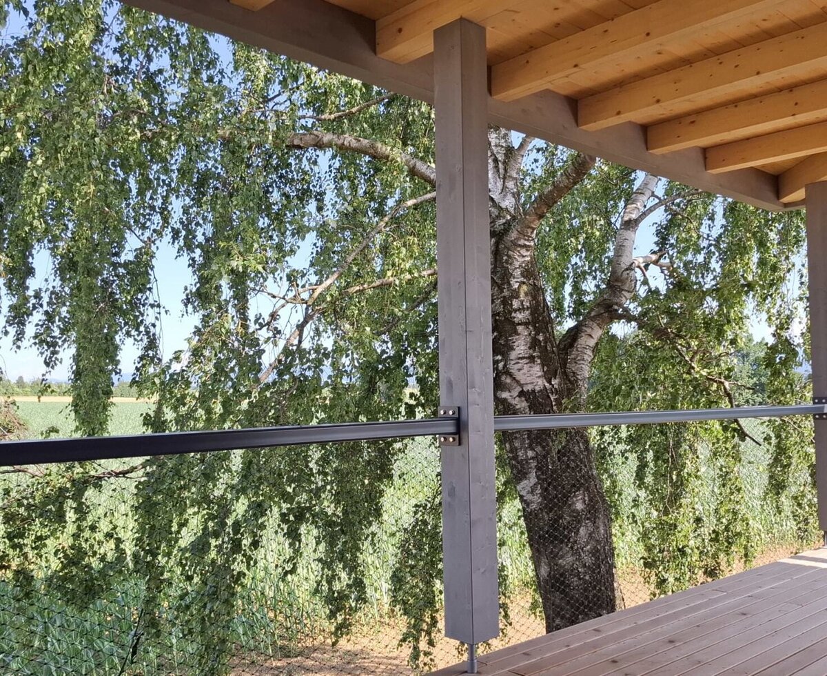 Balcony of the holiday home with a wooden floor and a view of a birch tree and fields.
