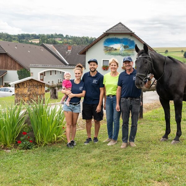 The welcoming host family greets you at their idyllic farmhouse, complete with horses and lush green pastures.