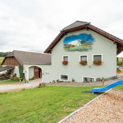 The inviting farmhouse featuring a spacious green lawn, a small children's playground, and a charming wall mural.