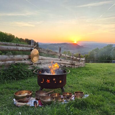 A cozy fire pit and singing bowls on the grassy lawn, set against an atmospheric sunset.
