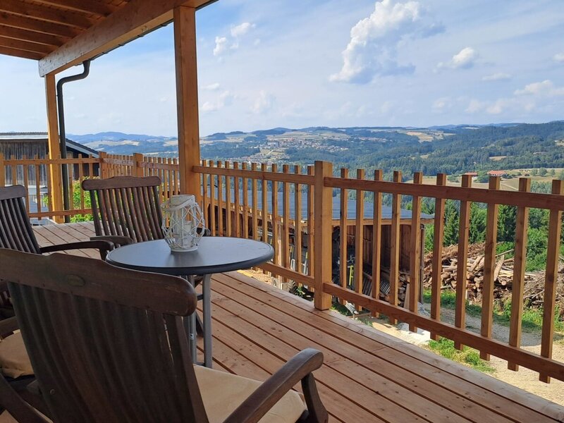 The inviting wooden terrace with cozy seating and a wide, panoramic view over the Mühlviertel landscape.
