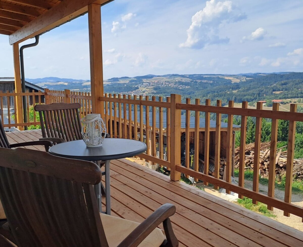 The inviting wooden terrace with cozy seating and a wide, panoramic view over the Mühlviertel landscape.