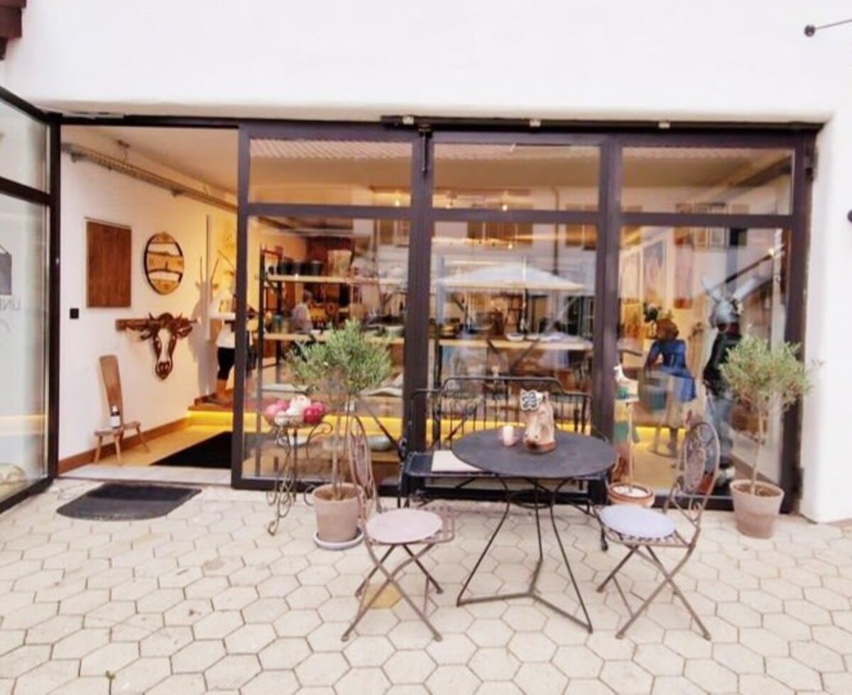 Outdoor seating area at the Farm House with a table and chairs, located in front of a shop entrance with glass doors.